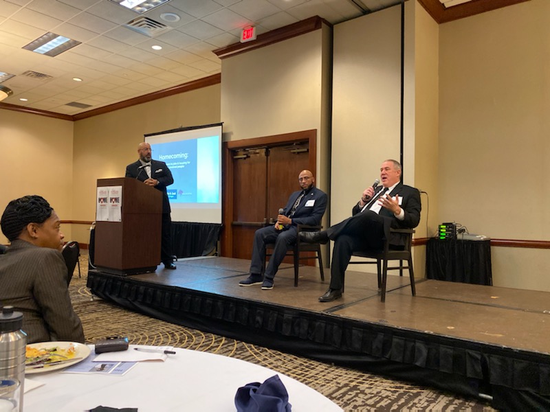 Joshua Hoe on the stage at a housing summit in Lansing Michigan discussing housing for formerly incarcerated people with Hakim Crampton and Troy Reinstra